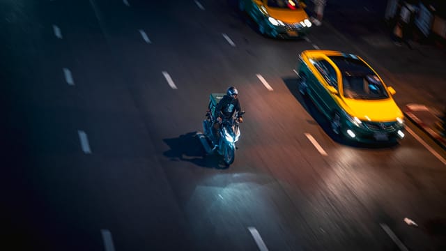 Nighttime aerial view of a bustling street in Kuwait City, showcasing motion blur of a motorbike and taxi.
