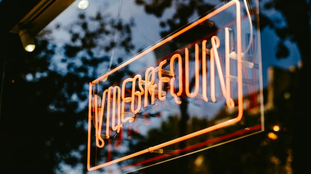 Close-up of an orange neon sign on a glass surface, creating an illuminated reflection.