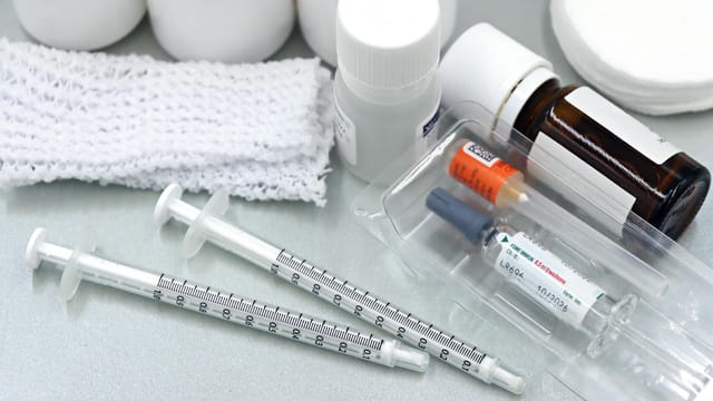 Flat lay of medical tools and vaccines, including syringes and bottles, on a white surface.