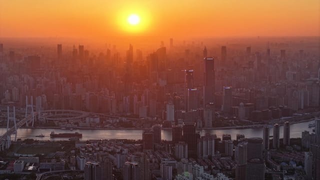 Aerial view of Shanghai's skyline at sunset with the Huangpu River reflecting the golden hues.