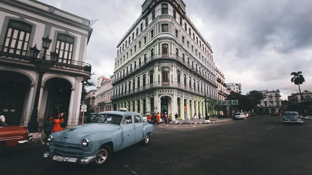 Classic cars drive past a historic building in Havana, Cuba's vibrant city center.