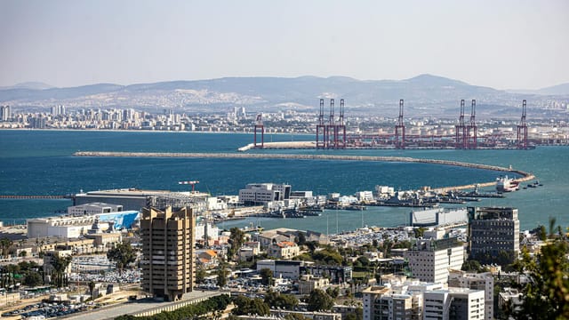 Panoramic view of Haifa port and cityscape against a mountainous backdrop on a sunny day.