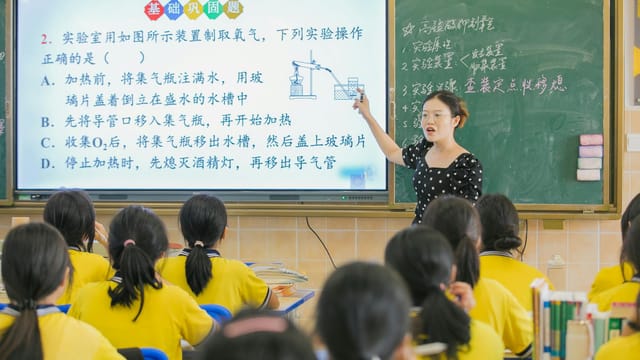 A teacher instructs students in a chemistry class, using a digital board for interactive learning.