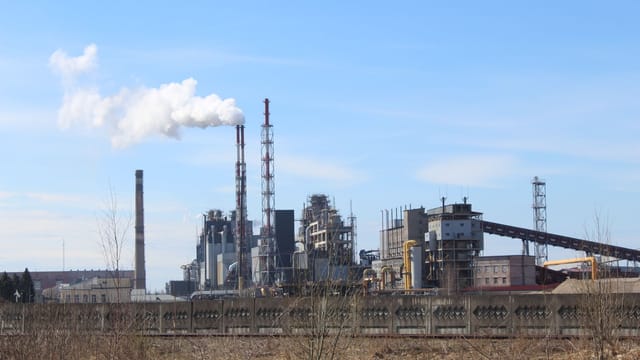 Illustrative image: An industrial factory with smoke emissions against a clear blue sky.