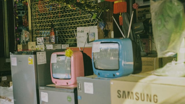 A storefront display featuring vintage televisions and home appliances on a sunny day in Bangkok.