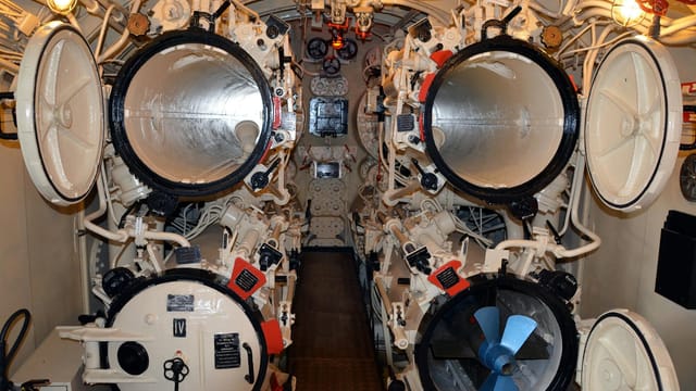 Detailed interior view of a submarine's torpedo room with open hatches.