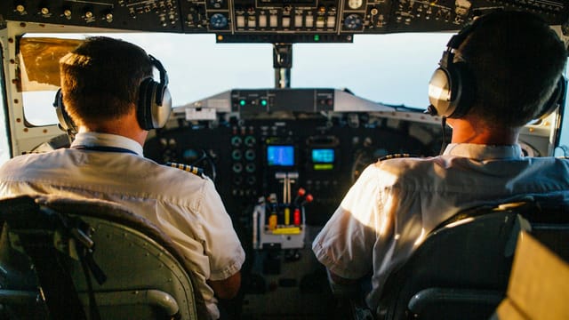 Two pilots in cockpit navigating airplane at high altitude, daylight