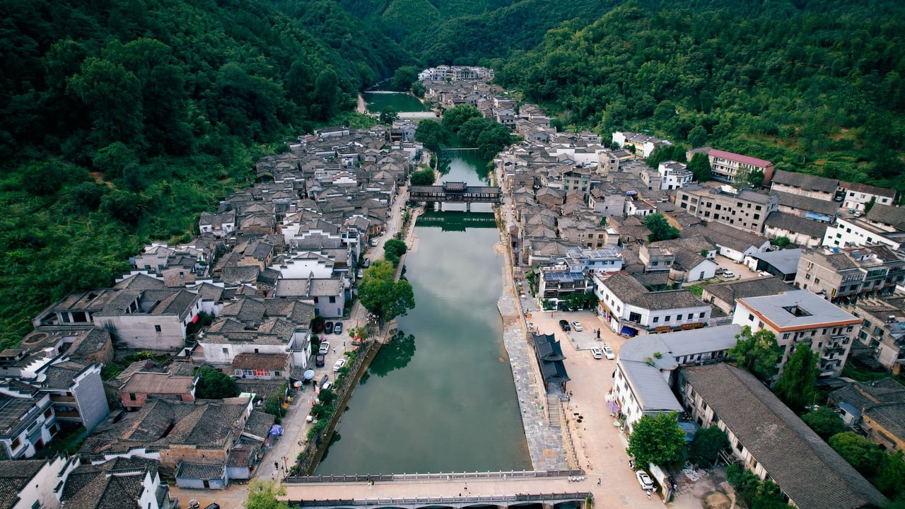 Aerial view of a historic village in Jiangxi, China surrounded by lush greenery and a tranquil river.