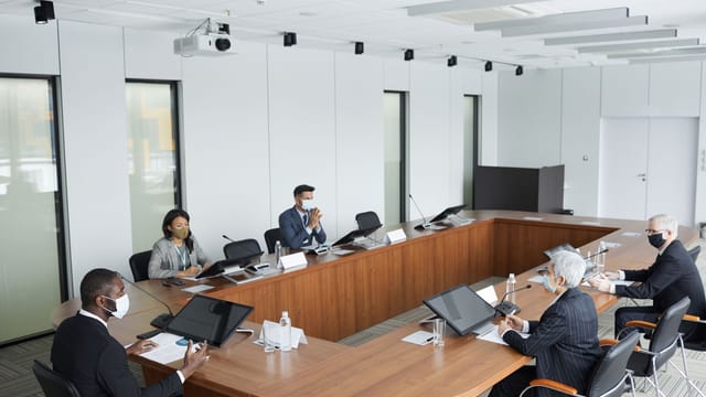 Business professionals wearing masks attending a conference meeting in a modern setting.