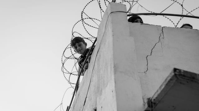 A child looks over a barbed-wire balcony, symbolizing hardship in Lebanon.