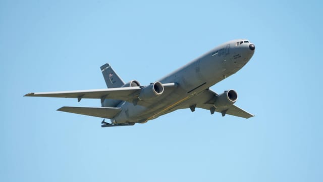 Aerial view of a large military aircraft flying over Fairfield, California under a clear blue sky.