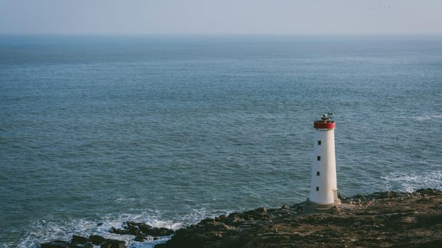 A white lighthouse stands on a rocky shore by the ocean in China, captured from an aerial view.