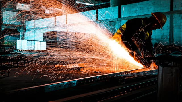 Illustrative image: An industrial worker using an angle grinder to cut steel, creating bright sparks in a factory setting.