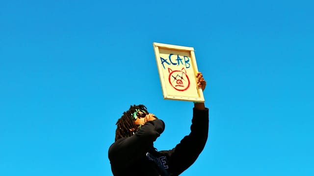 A protester raises a sign during a demonstration in Los Angeles under a clear blue sky.