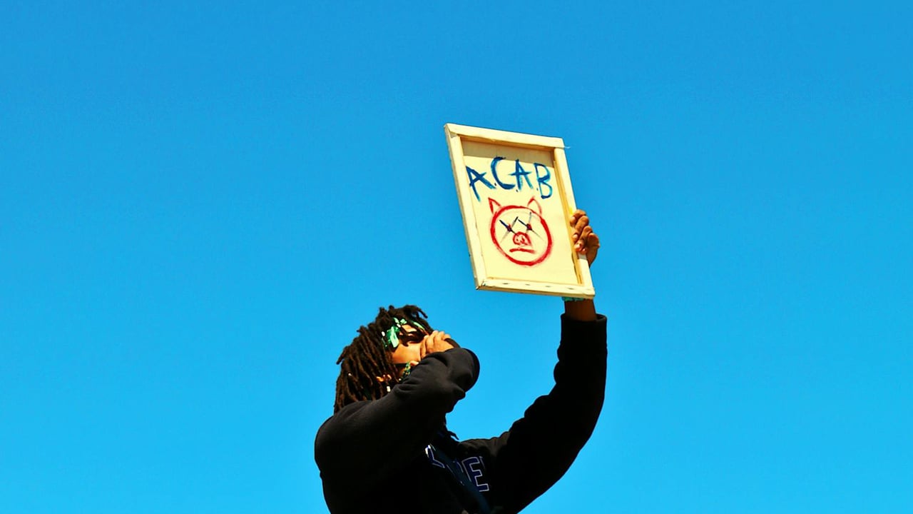 A protester raises a sign during a demonstration in Los Angeles under a clear blue sky.
