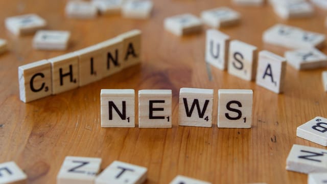Wooden Scrabble tiles spelling 'NEWS' with 'CHINA' and 'USA' on a wooden surface.