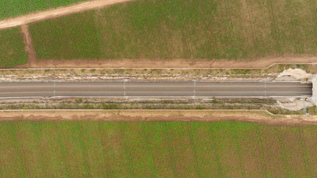Drone view of a railroad cutting through lush green farmland, illustrating rural infrastructure.