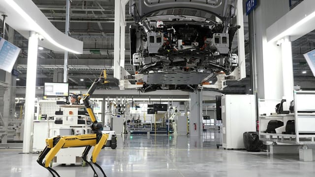 A robotic dog oversees an automated car assembly in a high-tech factory setting.