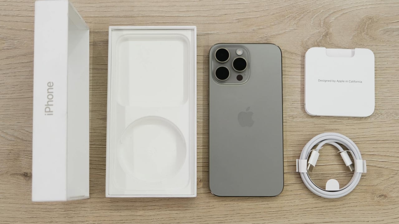 Flat lay view of the newest Apple iPhone model, box, and charging accessories on a wooden table.
