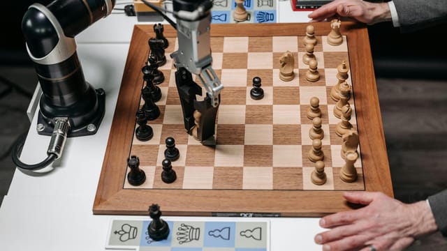 A robotic arm playing chess against a human hand on an electronic chessboard indoors.