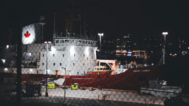Illuminated Canadian icebreaker ship docked in a harbor at night with city lights in the background.