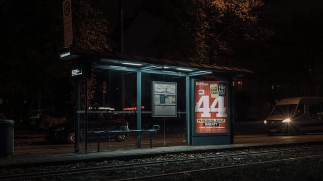 Quiet night scene of a tram stop in Munich showing an advertisement with a discount offer.