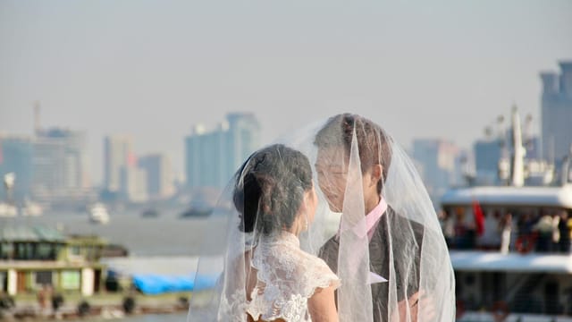 A romantic moment of a couple under a veil with a city skyline backdrop.