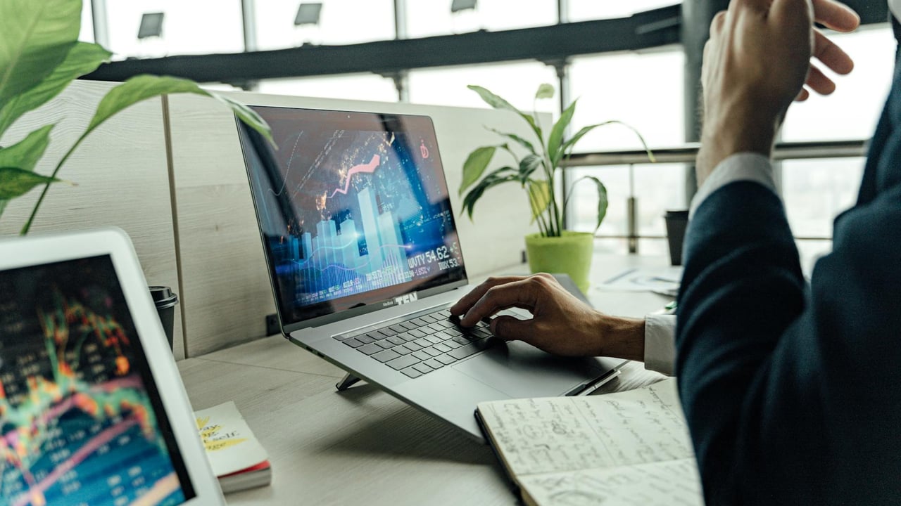 A professional analyzing stock market data on a laptop in a bright office environment.