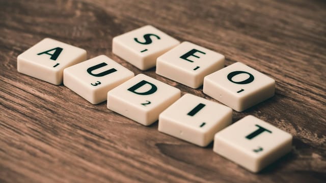 Scrabble tiles spelling SEO Audit on wooden surface, symbolizing digital marketing strategies.