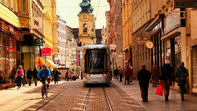 Urban street scene in Linz, Austria with tram, cyclists, and pedestrians.