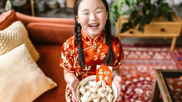 A smiling girl in a red cheongsam holds fortune cookies, celebrating Chinese New Year.