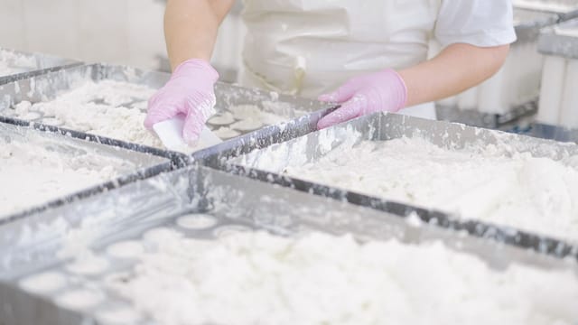 A person using pink gloves to prepare dough in a commercial baking facility.