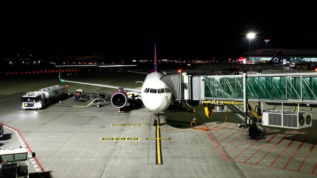 A large passenger airplane is docked at an airport terminal under night skies, ready for its next flight.