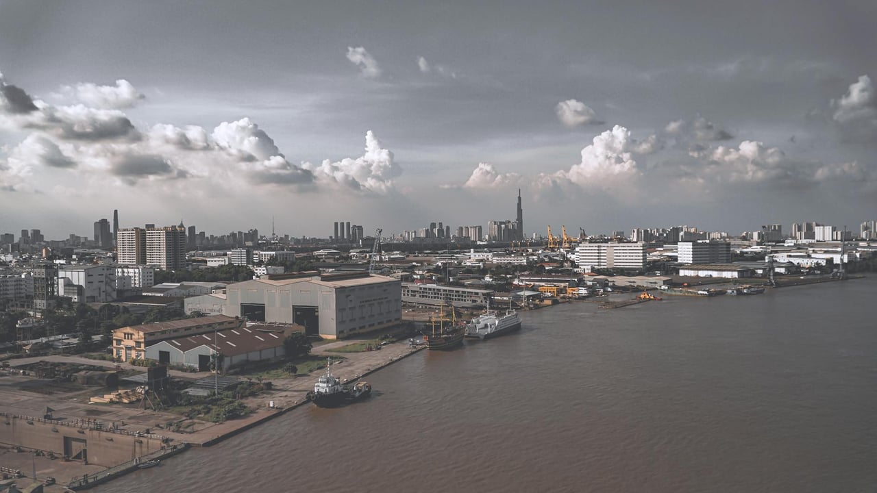Aerial shot of a bustling urban harbor with ships and buildings under a cloudy sky.