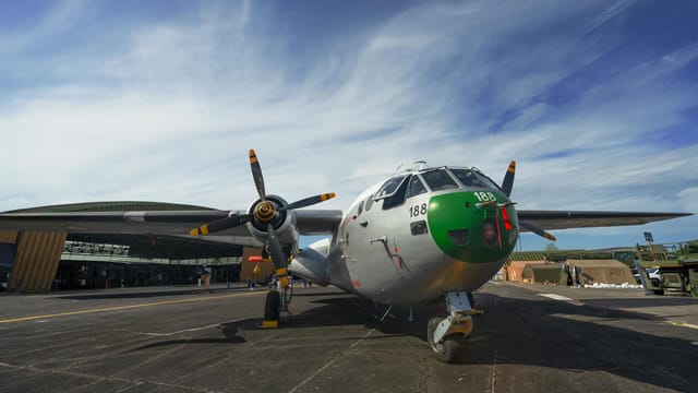 A military aircraft parked outdoors on an airbase under a bright blue sky.