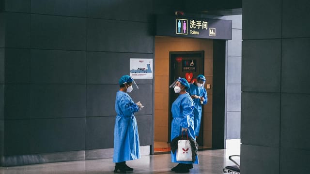 Medical professionals in protective gear near restroom in Shanghai building.