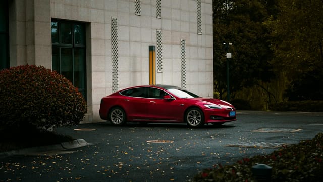 A stylish red electric car parked beside a modern building with landscaping and evening lighting.