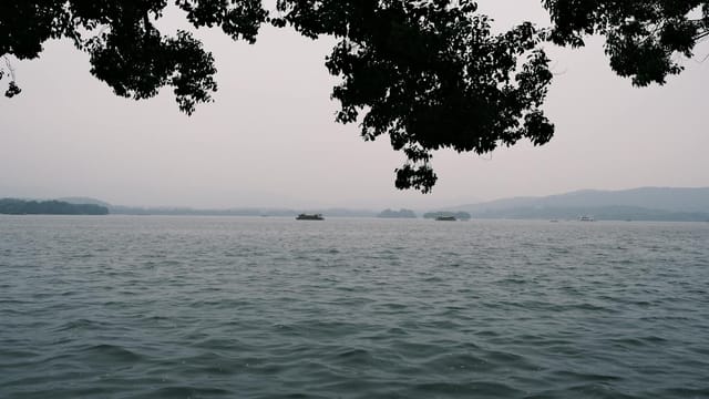 Tranquil scene of West Lake with peaceful waters and distant hills in Hangzhou, China.
