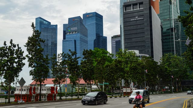 A view of Singapore's urban landscape featuring towering skyscrapers, bustling traffic, and a cyclist foreground.