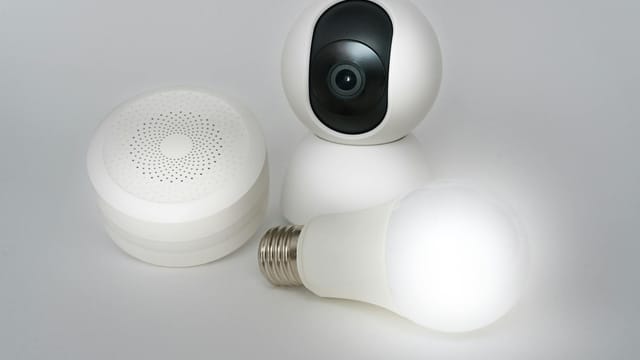 A set of smart home devices including a camera, speaker, and lightbulb on a white background.