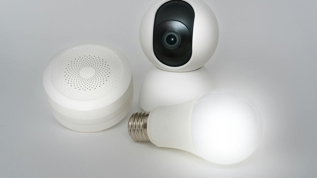 A set of smart home devices including a camera, speaker, and lightbulb on a white background.