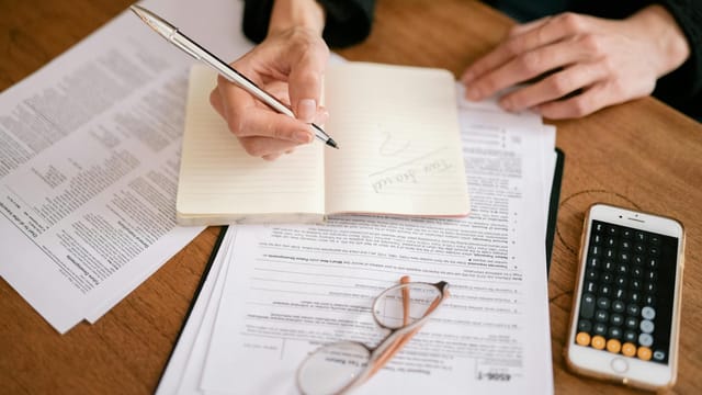 Close-up of a person writing in a notebook with documents and a calculator, managing finances.