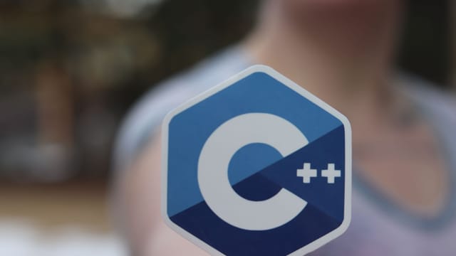 Close-up of person holding a C++ logo sticker, blurred background.
