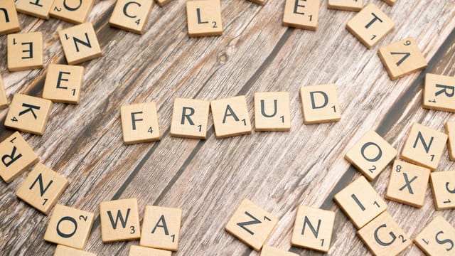 Alphabet tiles arranged to spell 'fraud' on a wooden surface, symbolizing deception.