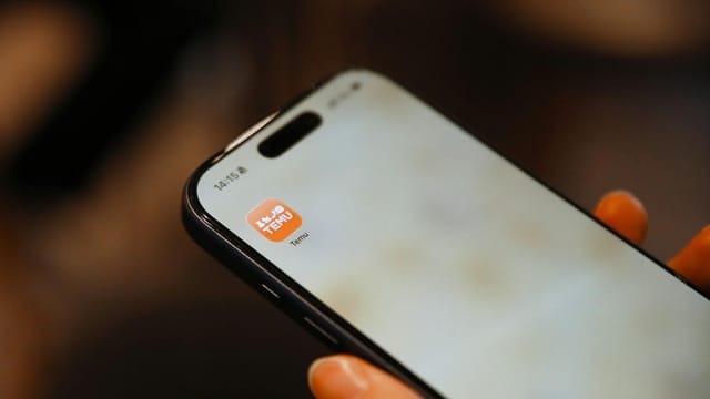 Hand holding smartphone with a shopping app icon visible, focusing on digital convenience.