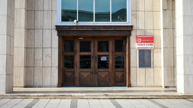 Wooden doors leading into a modern mosque facade, featuring traditional elements and contemporary design.
