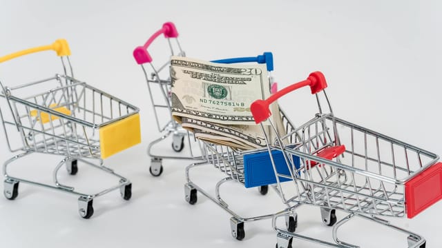 Miniature shopping carts containing dollar bills on a white background.