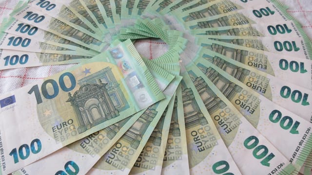 Close-up of a fan of 100 euro banknotes arranged in an artistic circle pattern on a textile surface.