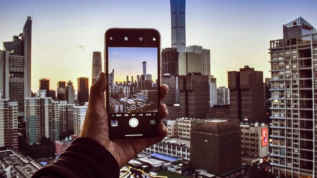 A hand holding a smartphone capturing the stunning Beijing skyline during sunset.