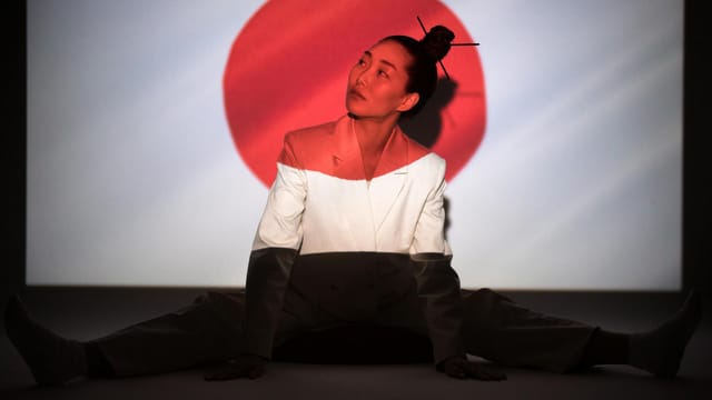 Asian woman poses with Japanese flag projection, embodying cultural symbolism.